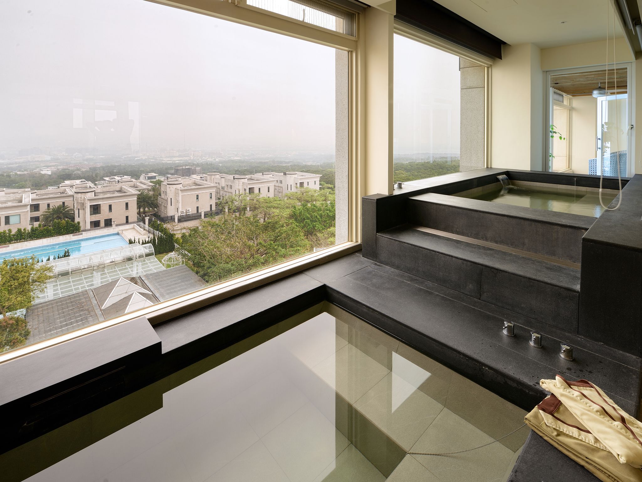 A modern bathroom with a large window, a built-in bathtub, and a view of a cityscape.