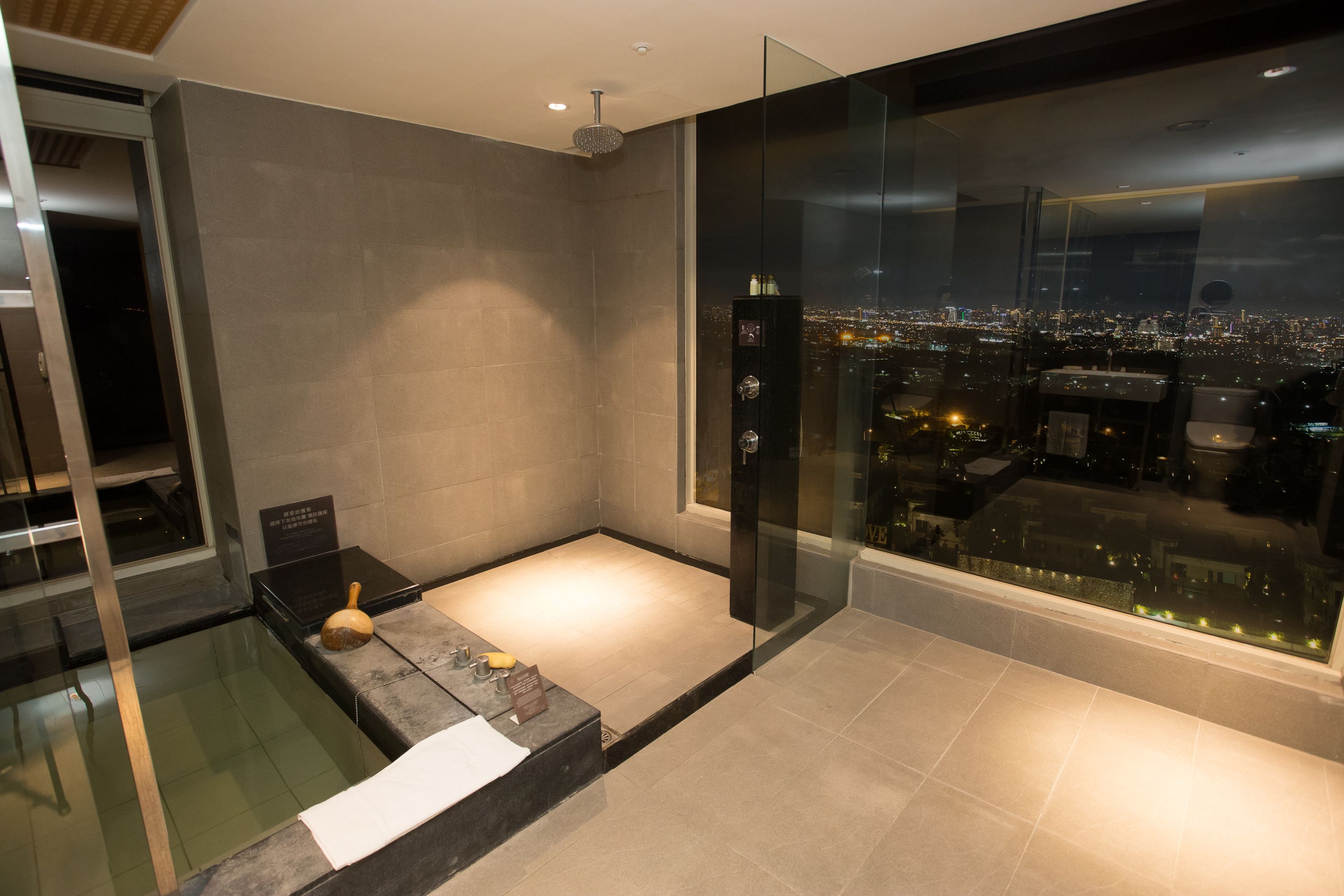 A modern bathroom with a glass shower enclosure, a bathtub, and a city view.