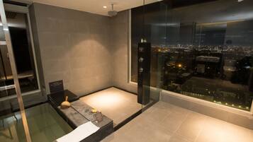A modern bathroom with a glass shower enclosure, a bathtub, and a city view.