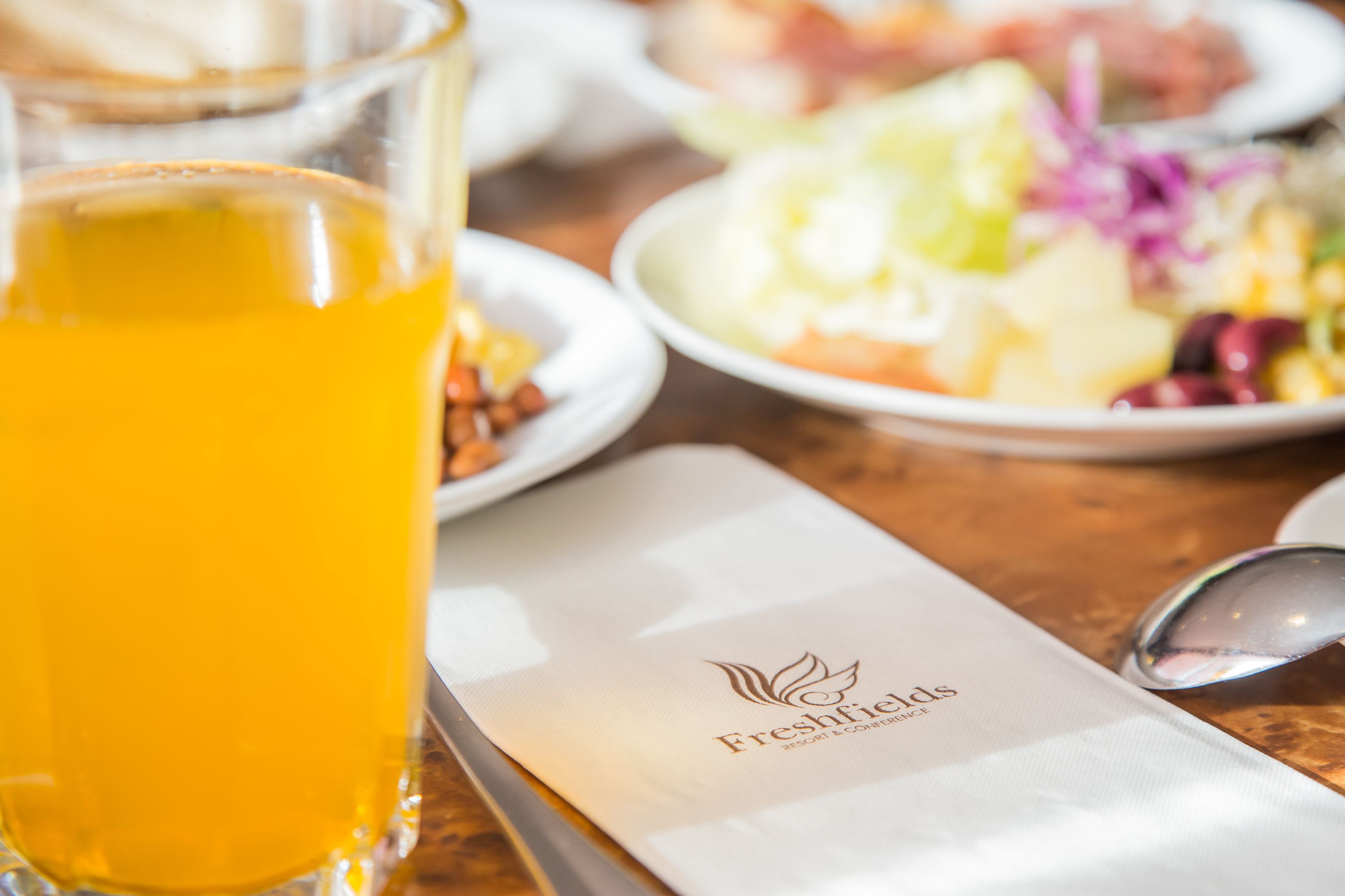 A table with a glass of orange juice, a spoon, and a menu with the logo "Freshfields Resort & Conference Centre".