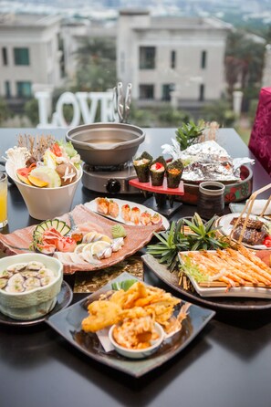 Taula amb diferents plats, incloent sushi, sashimi i tempura, amb un edifici al fons on es pot veure la paraula 'LOVE'.