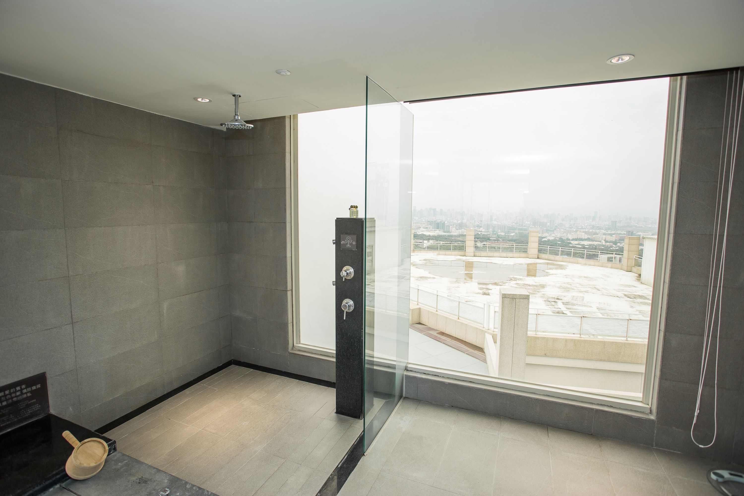 A modern bathroom with a glass shower enclosure, a bathtub, and a large window offering a city view.