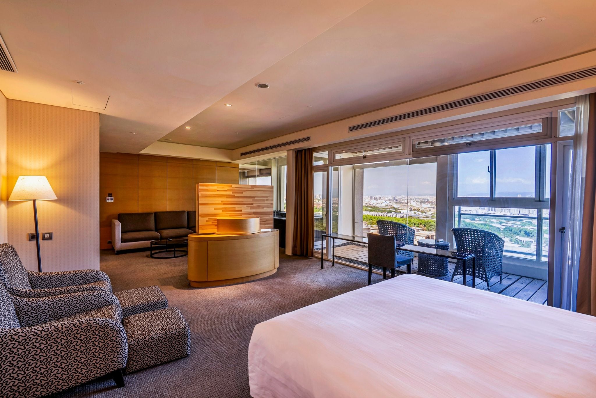 A hotel room with a bed, a sofa, a small table, and a balcony with a view.