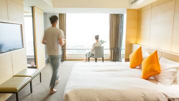 Habitación de hotel con una cama grande, televisión, banca y vistas al exterior.