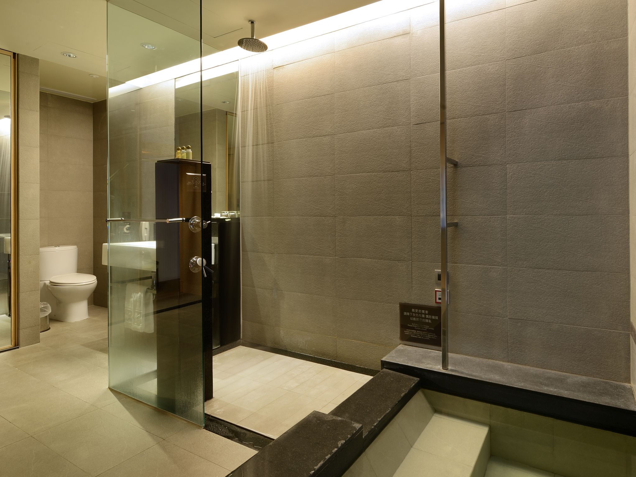 A modern bathroom with a glass-enclosed shower, a toilet, and a sink.