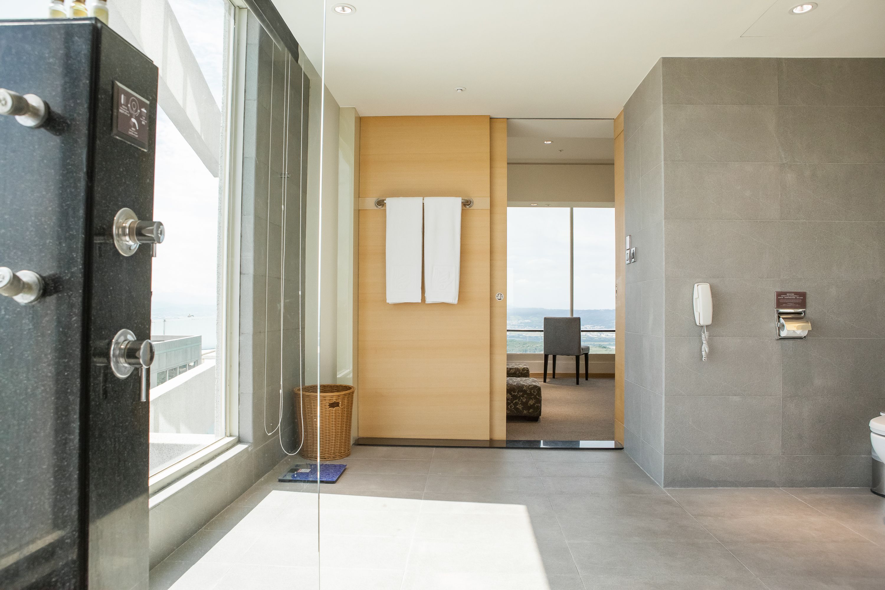 A modern hotel bathroom with a glass shower enclosure, a wooden door, and a view of the ocean.
