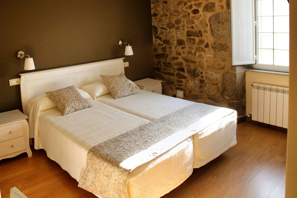 A bedroom with two beds, a stone wall, a window, and a ceiling light.