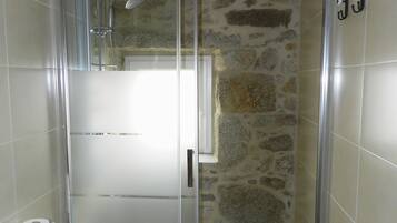 Une salle de bain avec une douche à parois de verre, des toilettes et un mur en pierre.