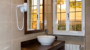A bathroom with a white sink, wooden vanity, a mirror with lights, a window, and a toilet.