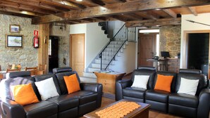 A spacious living area with leather sofas, a coffee table, and a staircase leading to an upper floor. - A Casa do Folgo (A Baña)