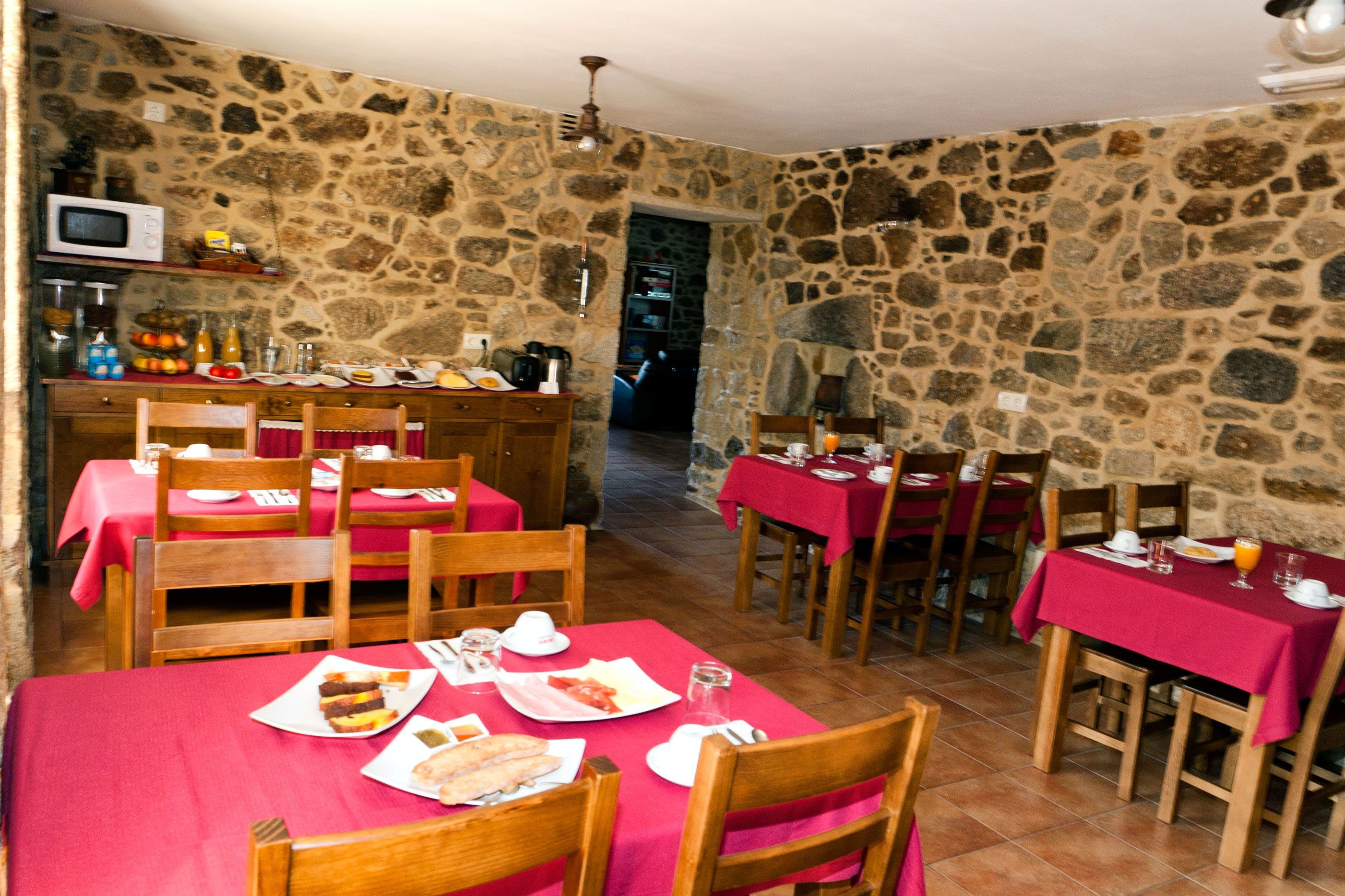 A dining area with stone walls, wooden tables and chairs, and a red tablecloth.