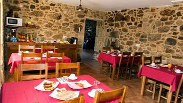 A dining area with stone walls, wooden tables and chairs, and a red tablecloth.