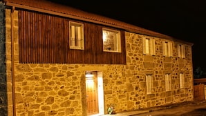 A stone building with a wooden door and windows, illuminated at night. - A Casa do Folgo (A Baña)