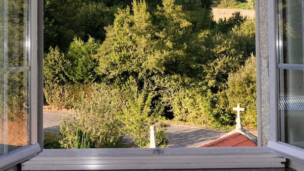 A view from a window overlooking a forested area with a cross on a roof. - A Casa do Folgo (A Baña)