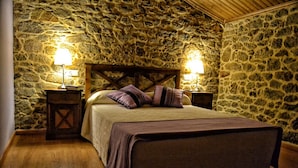 A bedroom with a stone wall, wooden headboard, and two bedside tables with lamps. - A Casa do Folgo (A Baña)