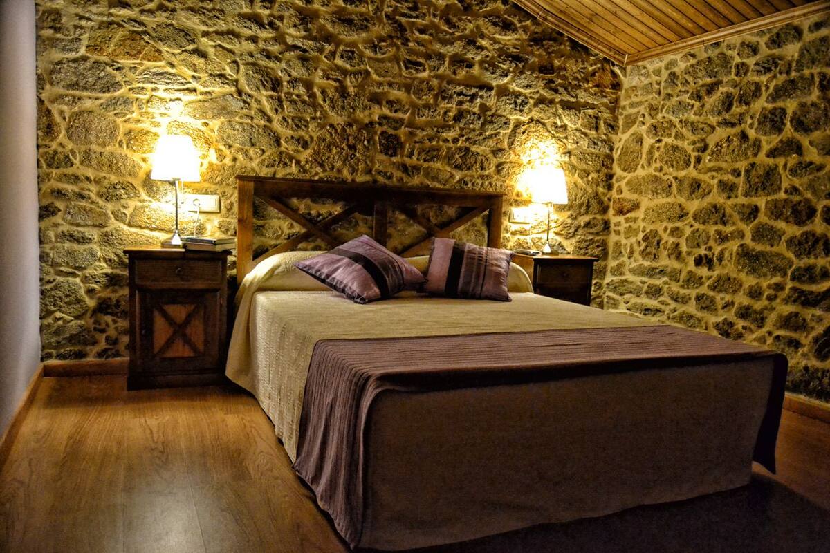 A bedroom with a stone wall, wooden headboard, and two bedside tables with lamps.