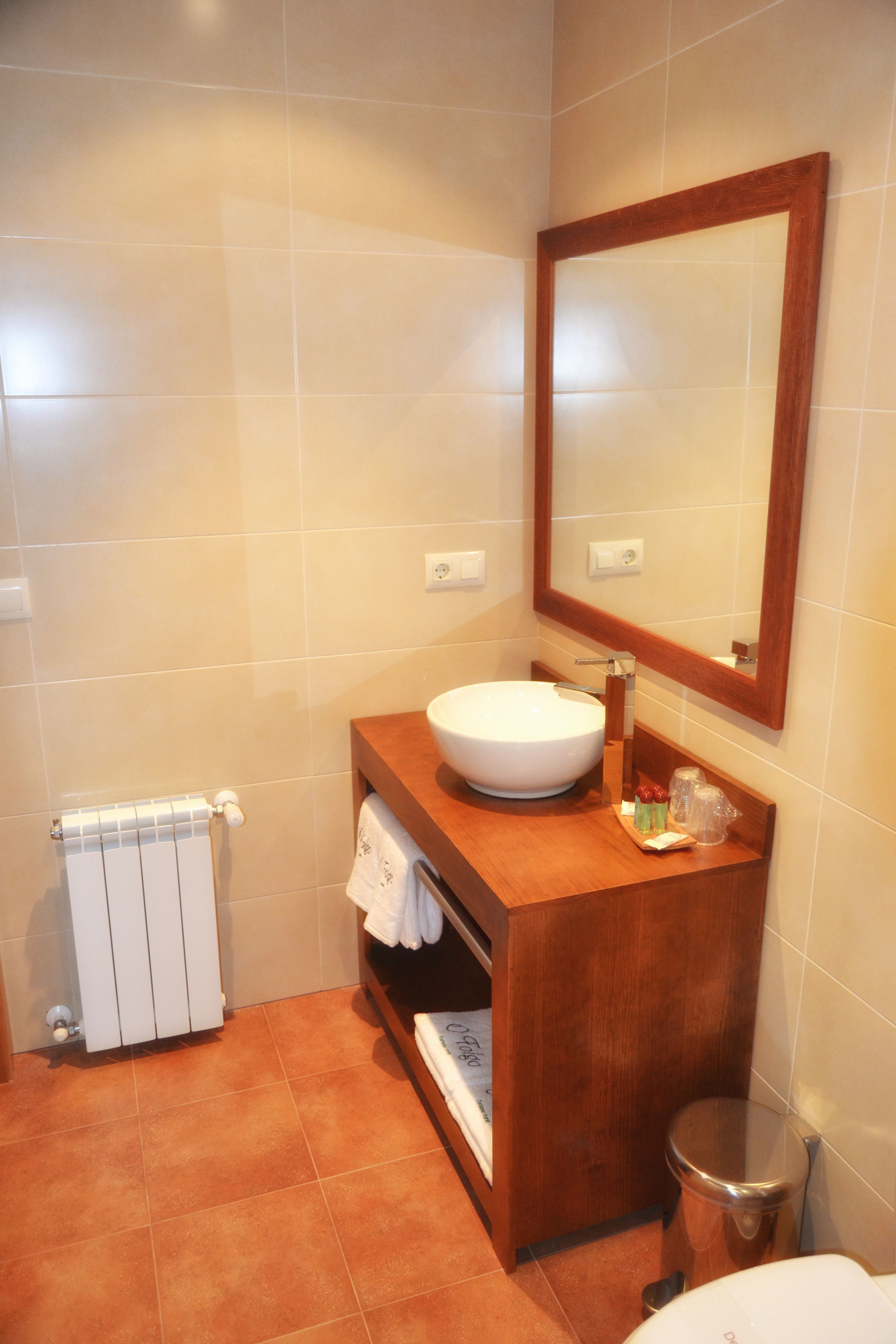 A bathroom with a wooden vanity, a white sink, a mirror, a towel rack, and a radiator.