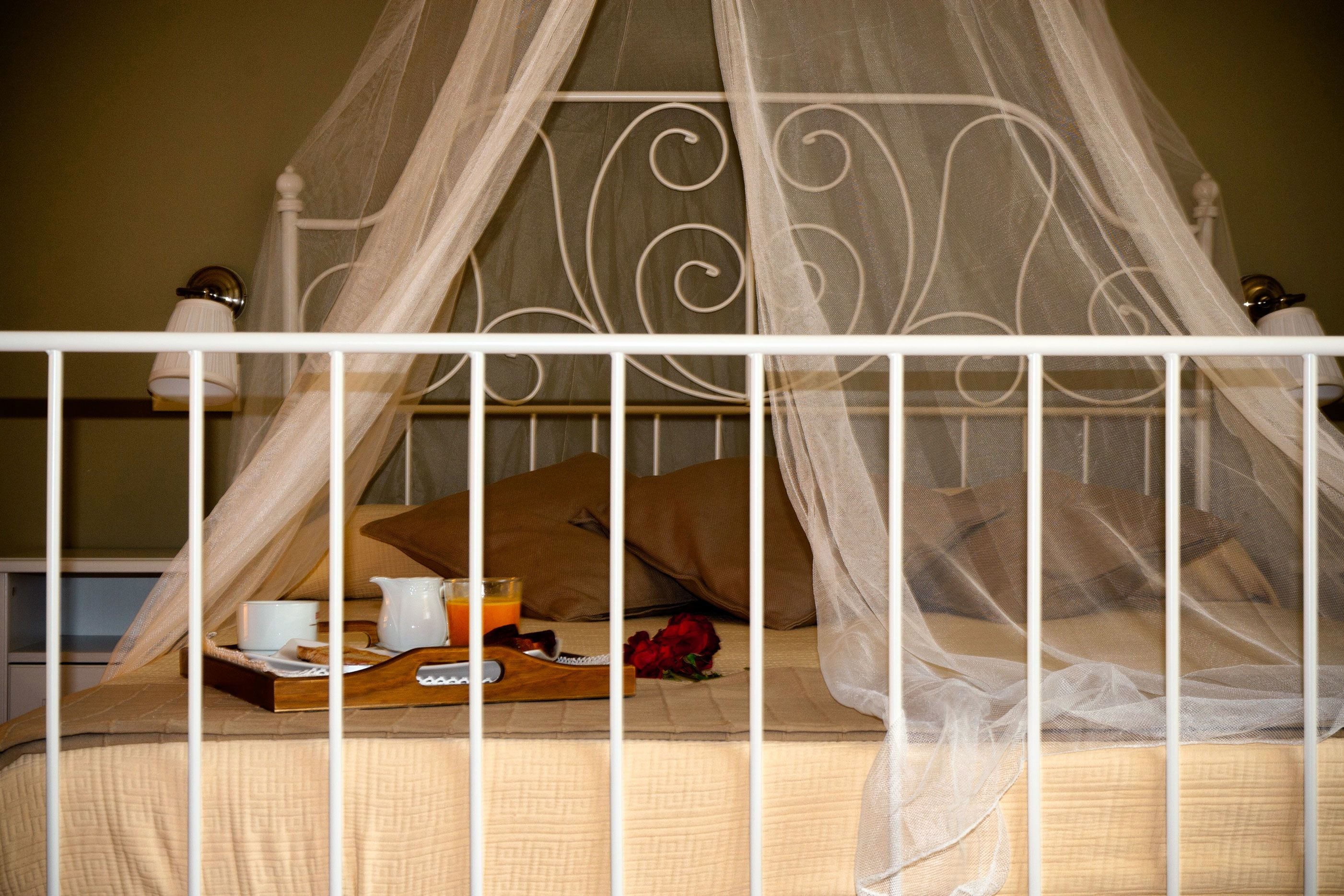 Una cama con dosel y cuatro columnas con una bandeja de desayuno, un jarro de zumo de naranja y una rosa roja sobre la cama.