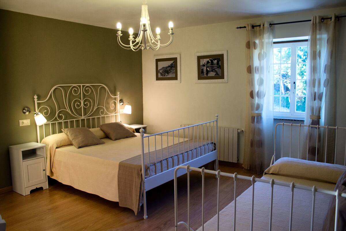 A bedroom with a metal bed frame, a nightstand, a bedside lamp, and a window with curtains.