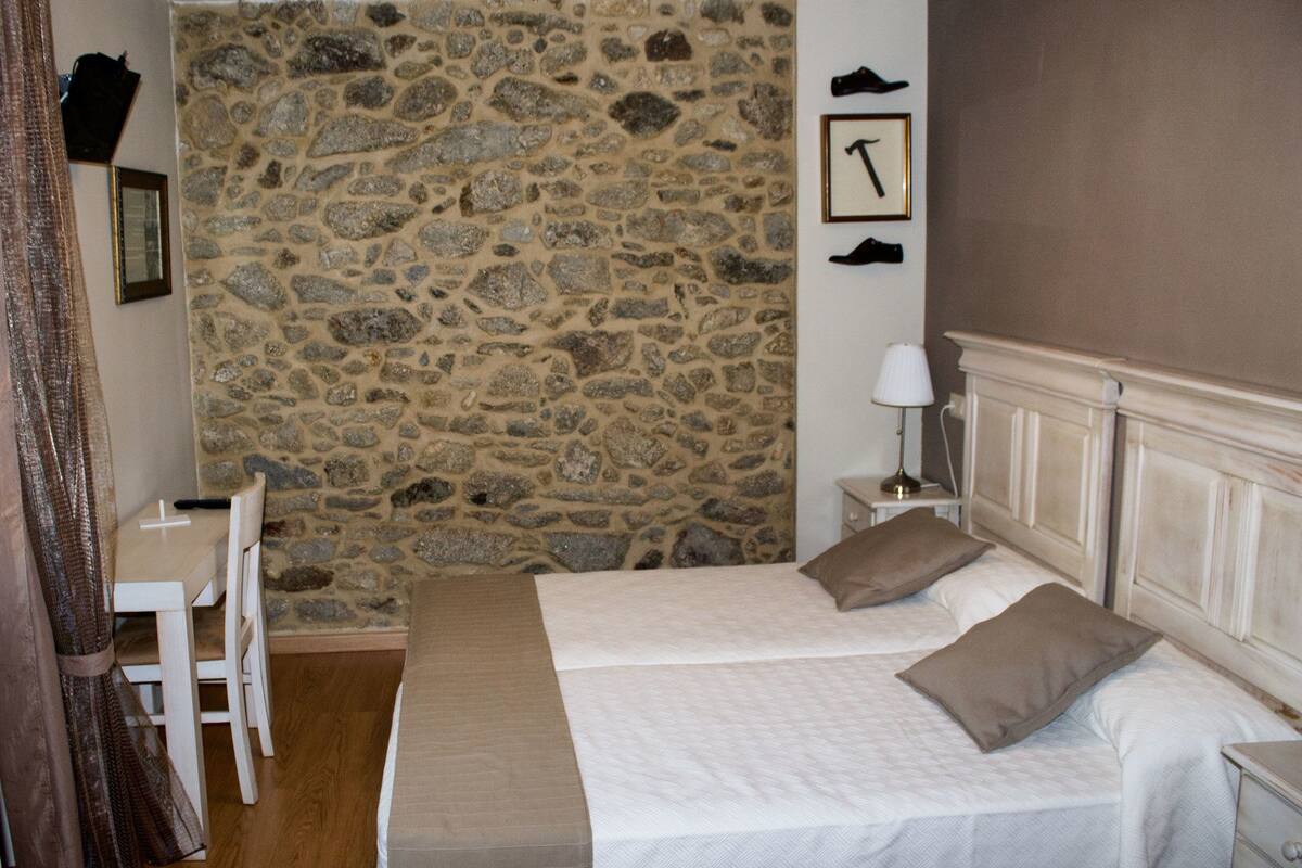 A bedroom with a stone wall, two beds, a desk, and a nightstand.
