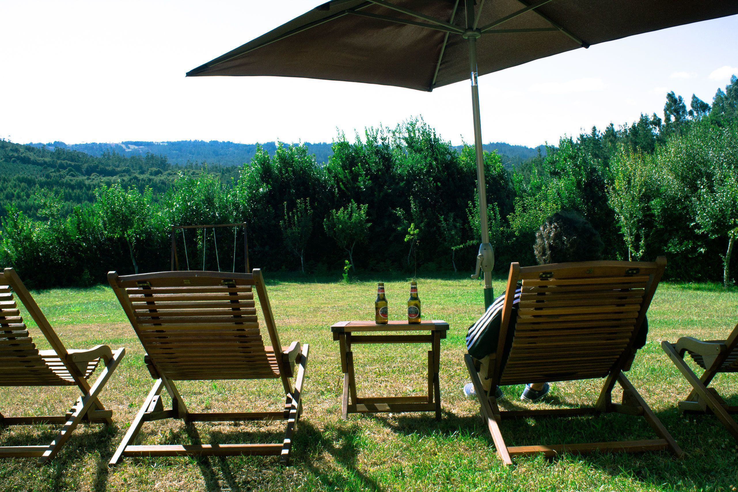 Drie houten lounge fauteuils onder een grote parasol, met een klein tafeltje ertussen.