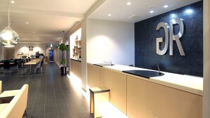 Un hall d’hôtel moderne avec un comptoir d’accueil, un espace salon et une horloge au mur.