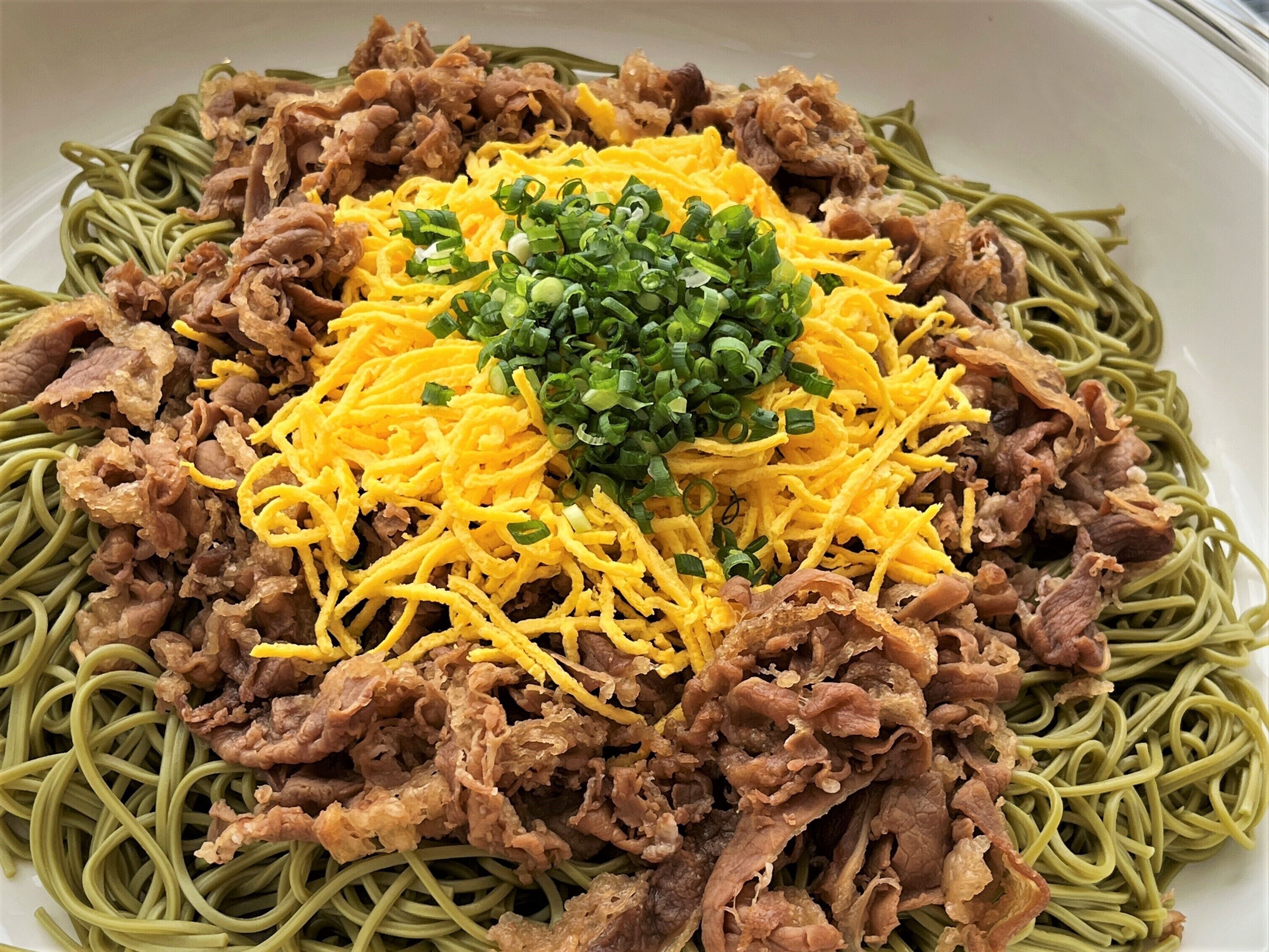 A plate of spaghetti with shredded cheese, green onions, and fried meat.