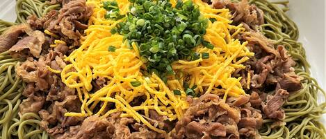 A plate of spaghetti with shredded cheese, green onions, and fried meat.