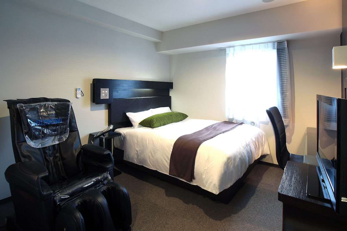 A hotel room with a bed, a desk, a chair, a TV, and a massage chair.