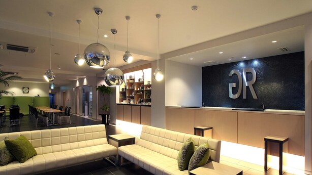 Un hall d’hôtel moderne, doté d’un espace salon, d’un comptoir d’accueil et d’un panneau « R » bien visible sur le mur.