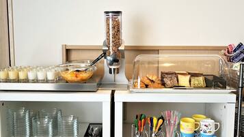 Un bufé de desayuno con cereales, leche y bollería.
