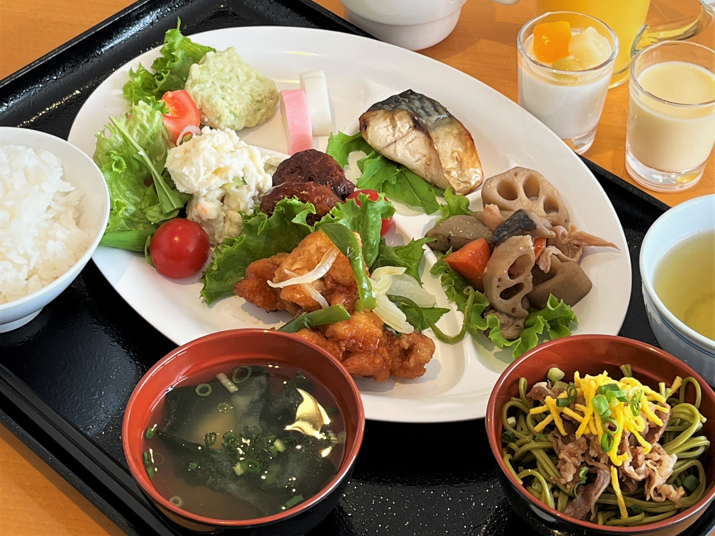 A tray with a plate of food including rice, salad, fish, and soup.