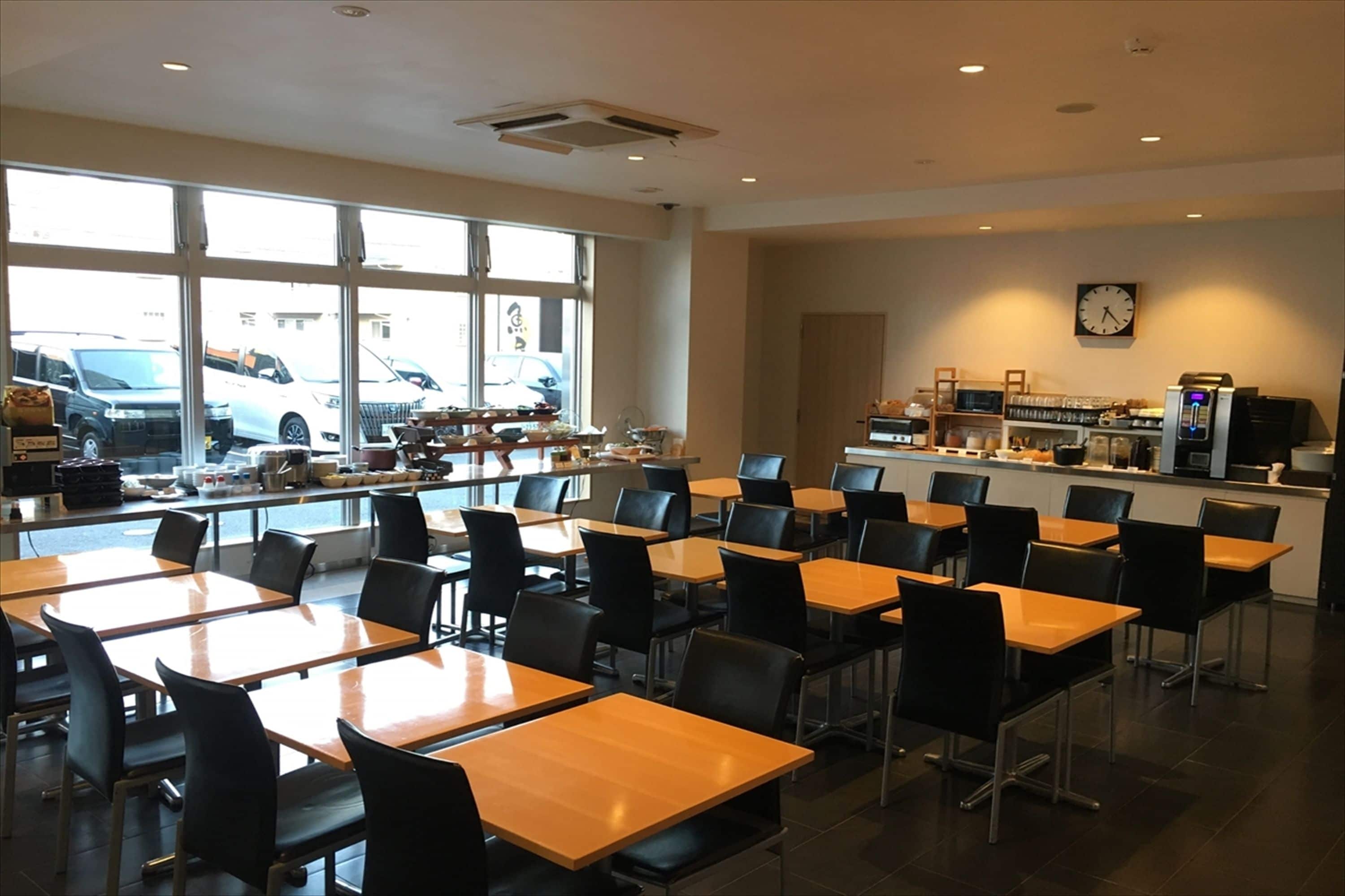 A spacious dining area with multiple tables and chairs, a coffee machine, and a view of parked cars outside.