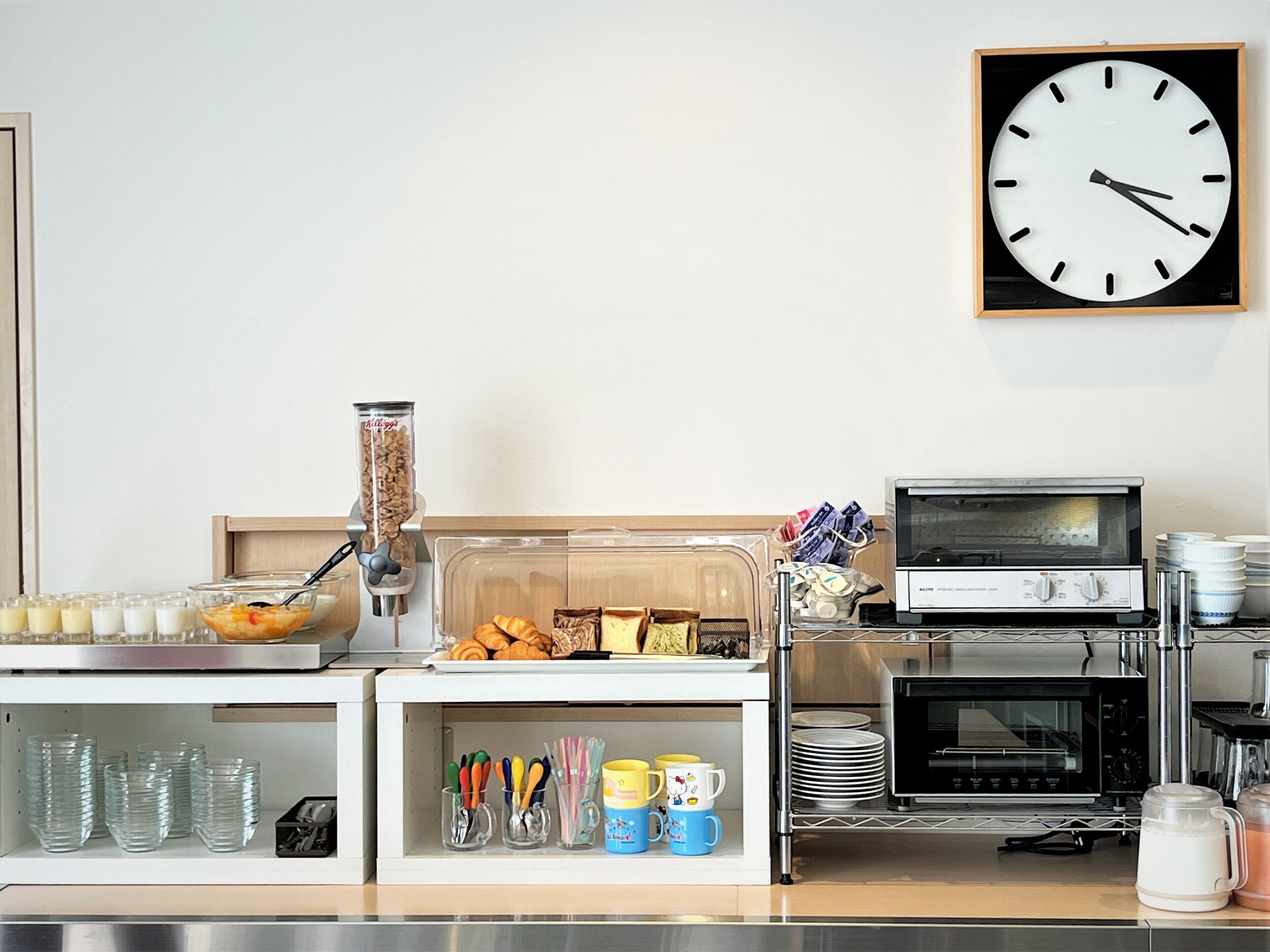 A breakfast bar with a coffee machine, cereal dispenser, and a variety of food items. There is a microwave, toaster, and a coffee maker on the counter.