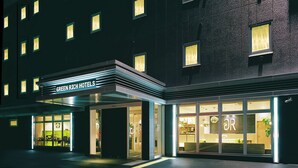 L’extérieur d’un hôtel de nuit, avec une enseigne lumineuse, de grandes fenêtres et un espace de réception bien visible.