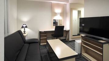Una habitación de hotel con sofá, escritorio, televisión y lámpara.