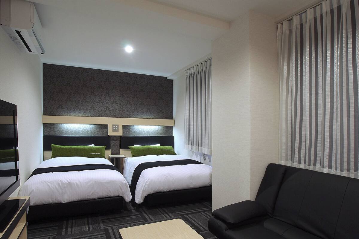 Een hotelkamer met twee bedden, een bank, een kleine tafel en een groot raam met gordijnen.