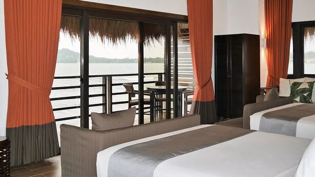 A hotel room with two beds, a balcony with a table and chairs, and a view of the water. - Matabungkay Beach Hotel (Lian)