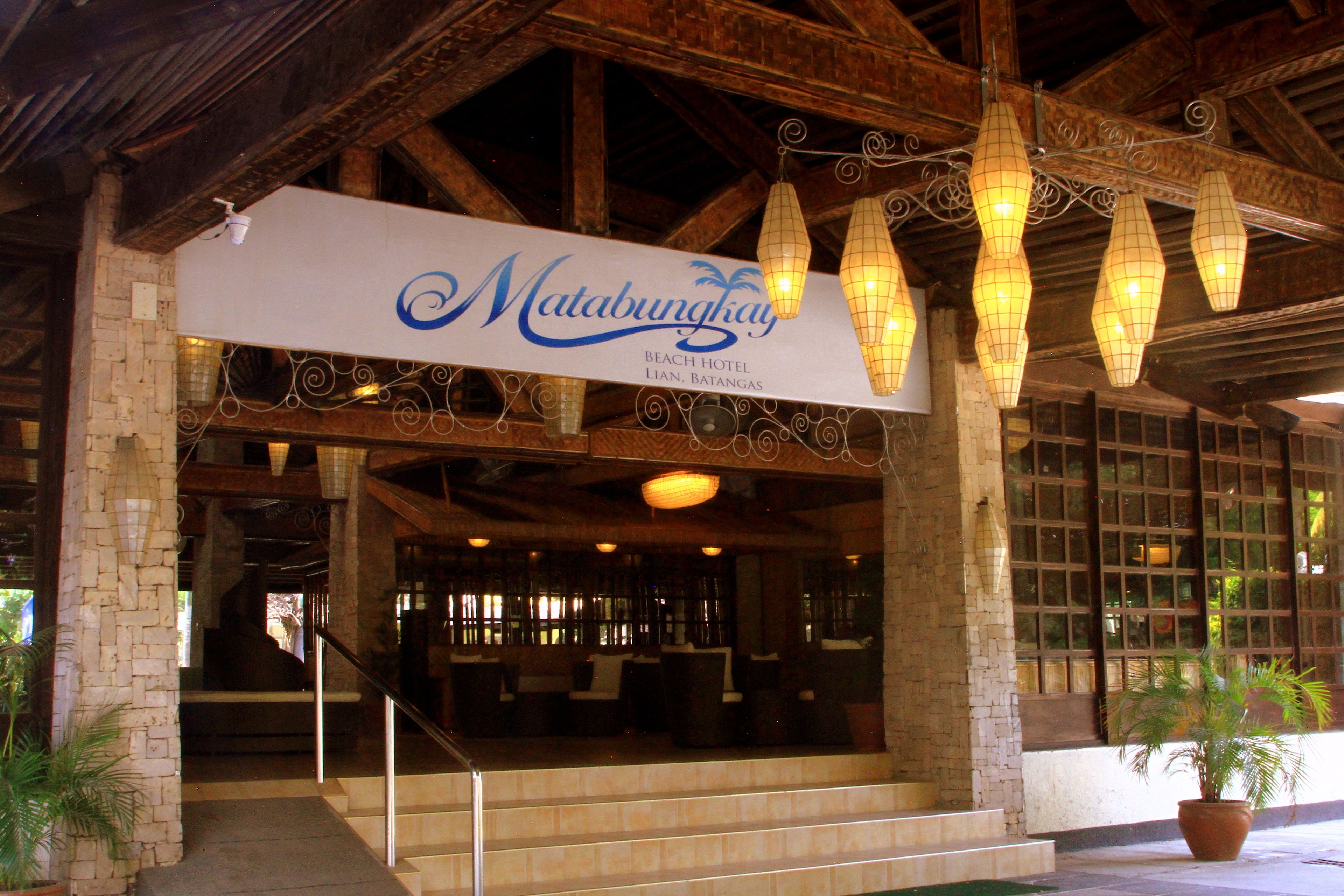 The entrance of Matabungkay Beach Hotel with a sign, wooden beams, and hanging light fixtures.