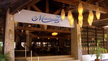 The entrance of Matabungkay Beach Hotel with a sign, wooden beams, and hanging light fixtures.
