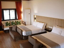 Habitación de hotel con dos camas, un sofá, una mesita y una ventana con cortinas.