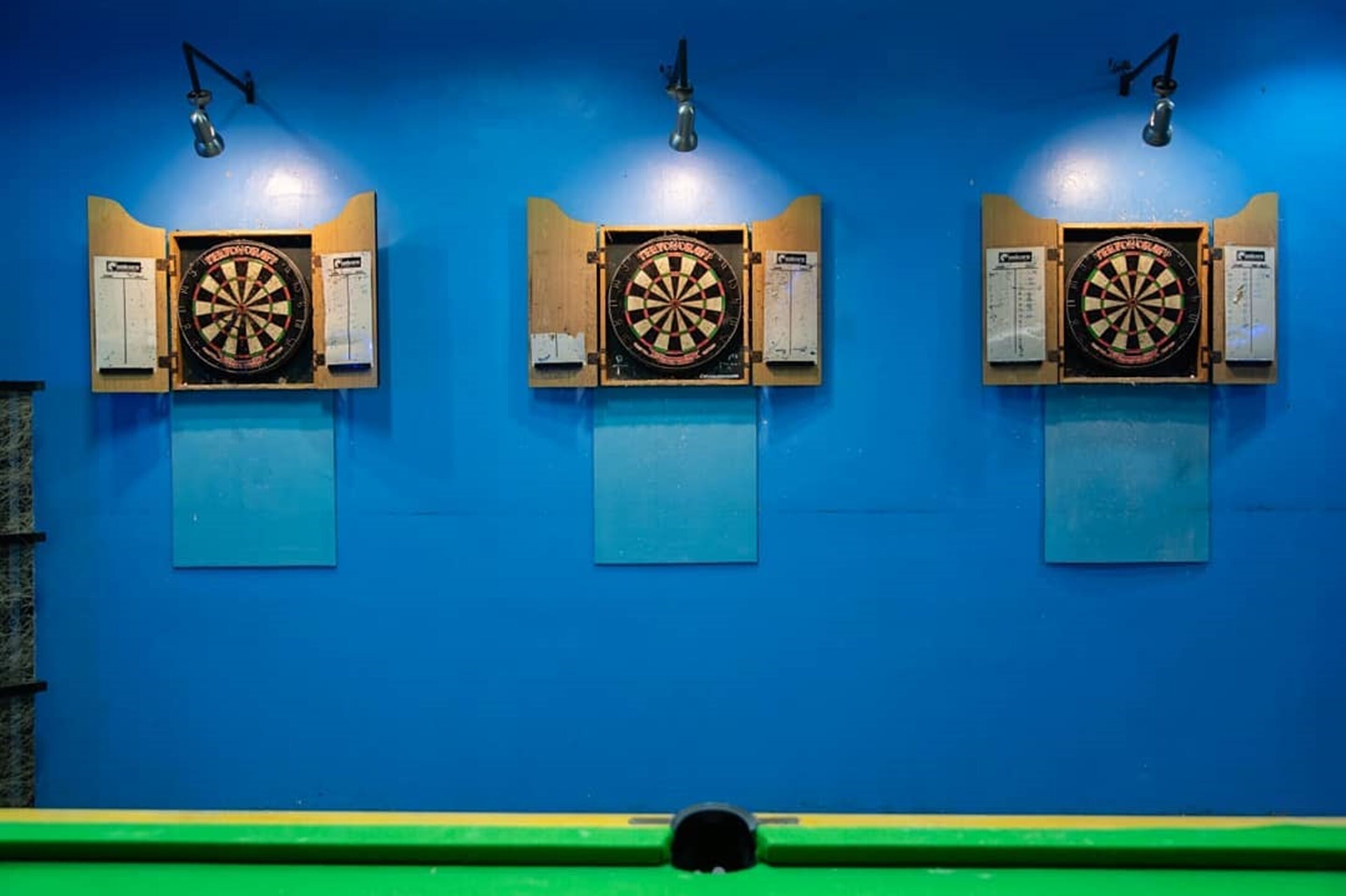 Three dartboards mounted on a blue wall with scoreboards below each.