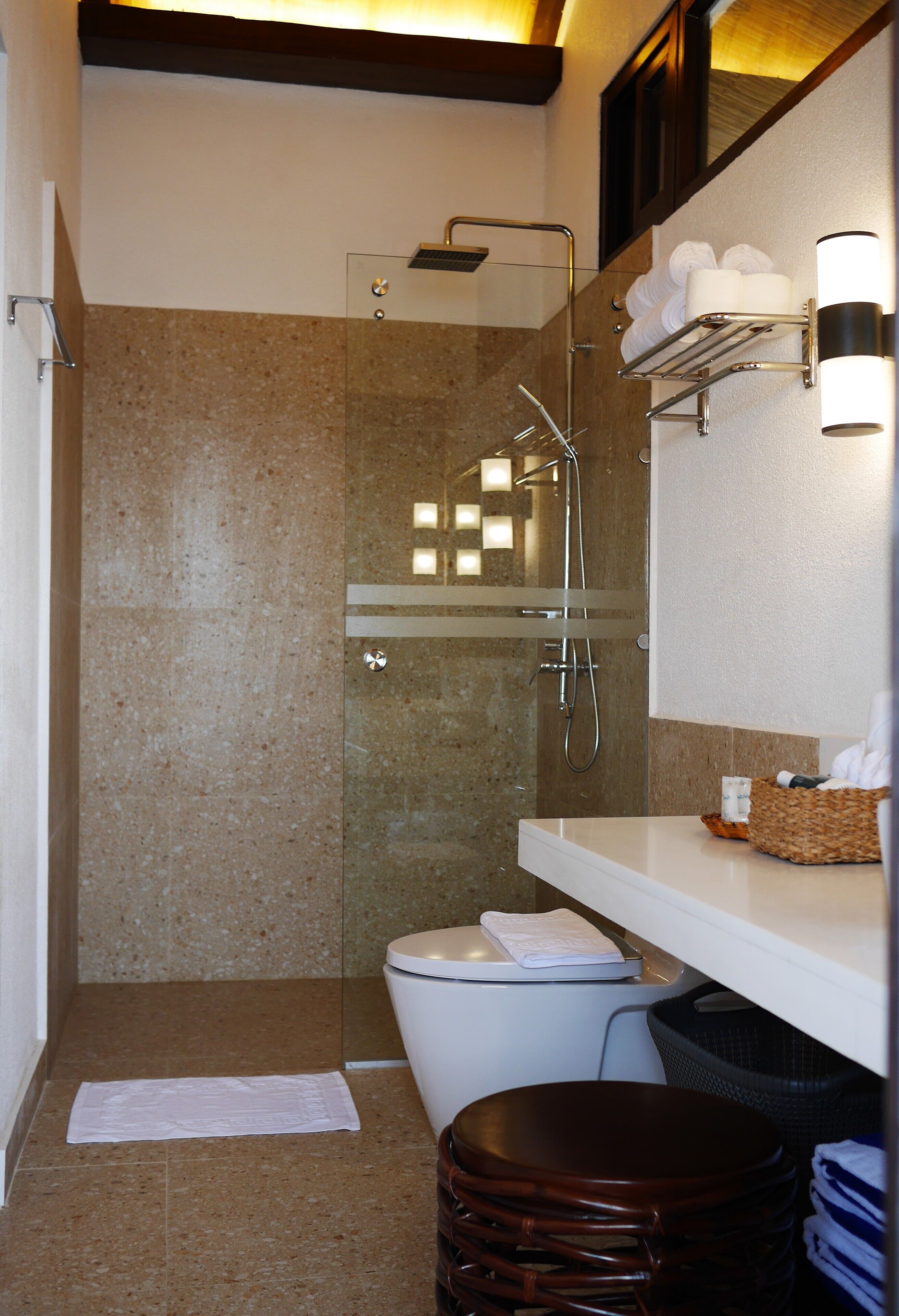 Une salle de bain moderne avec une douche à parois de verre, des toilettes blanches, un meuble-lavabo avec un porte-serviettes et un petit tabouret.