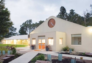 A modern building with a circular window and a door, surrounded by landscaped gardens and a pathway. - Foothills Conference Centre (Mooroolbark)
