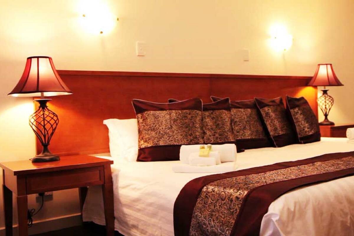 Una habitación de hotel con una cama grande, dos lámparas de noche, un cabecero y una mesita de noche.