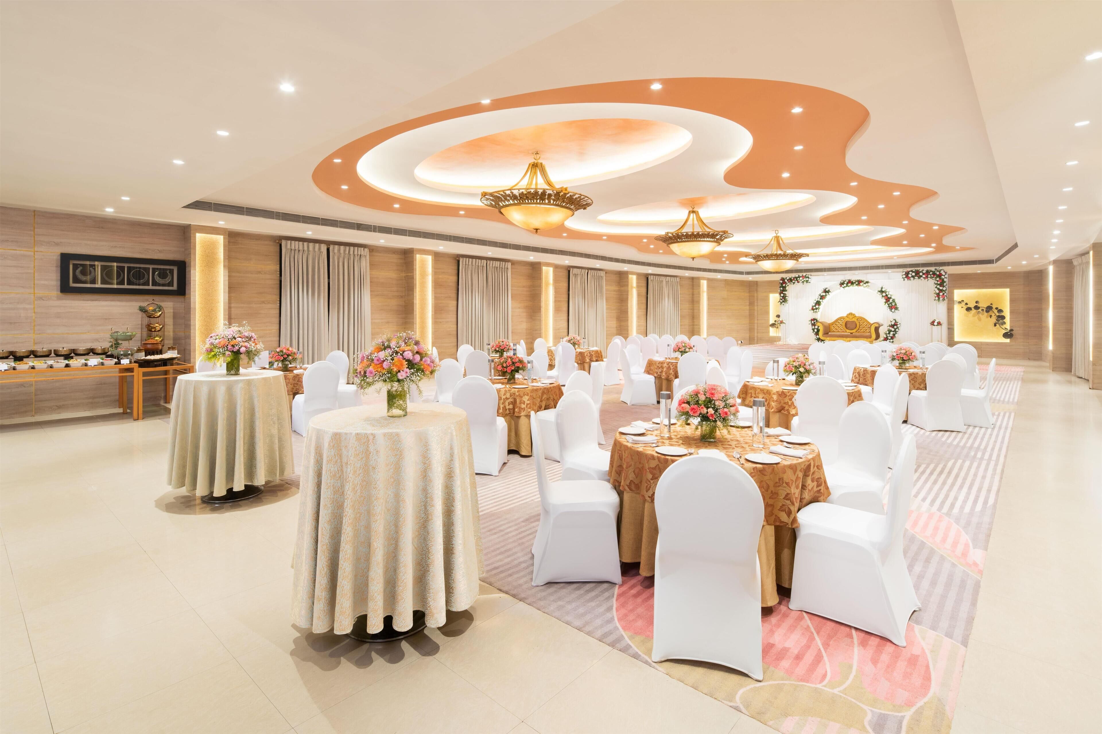 Een feestzaal met ronde tafels, witte stoelen en bloemstukken.