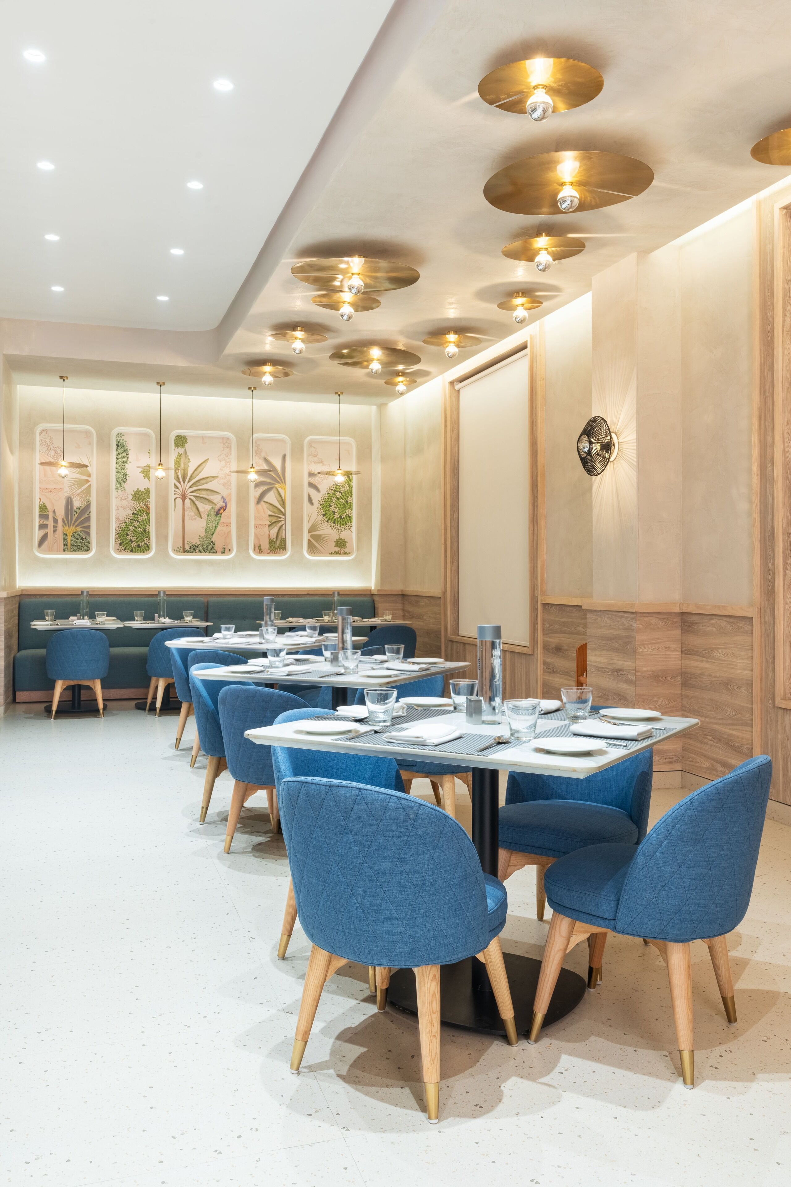 A modern dining area with round tables, blue upholstered chairs, and recessed ceiling lighting.