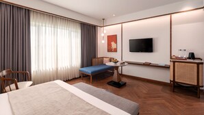 A hotel room with a bed, a desk, a chair, a television, and a window with curtains. - Nidhivan Sarovar Portico Vrindavan (Mathura)