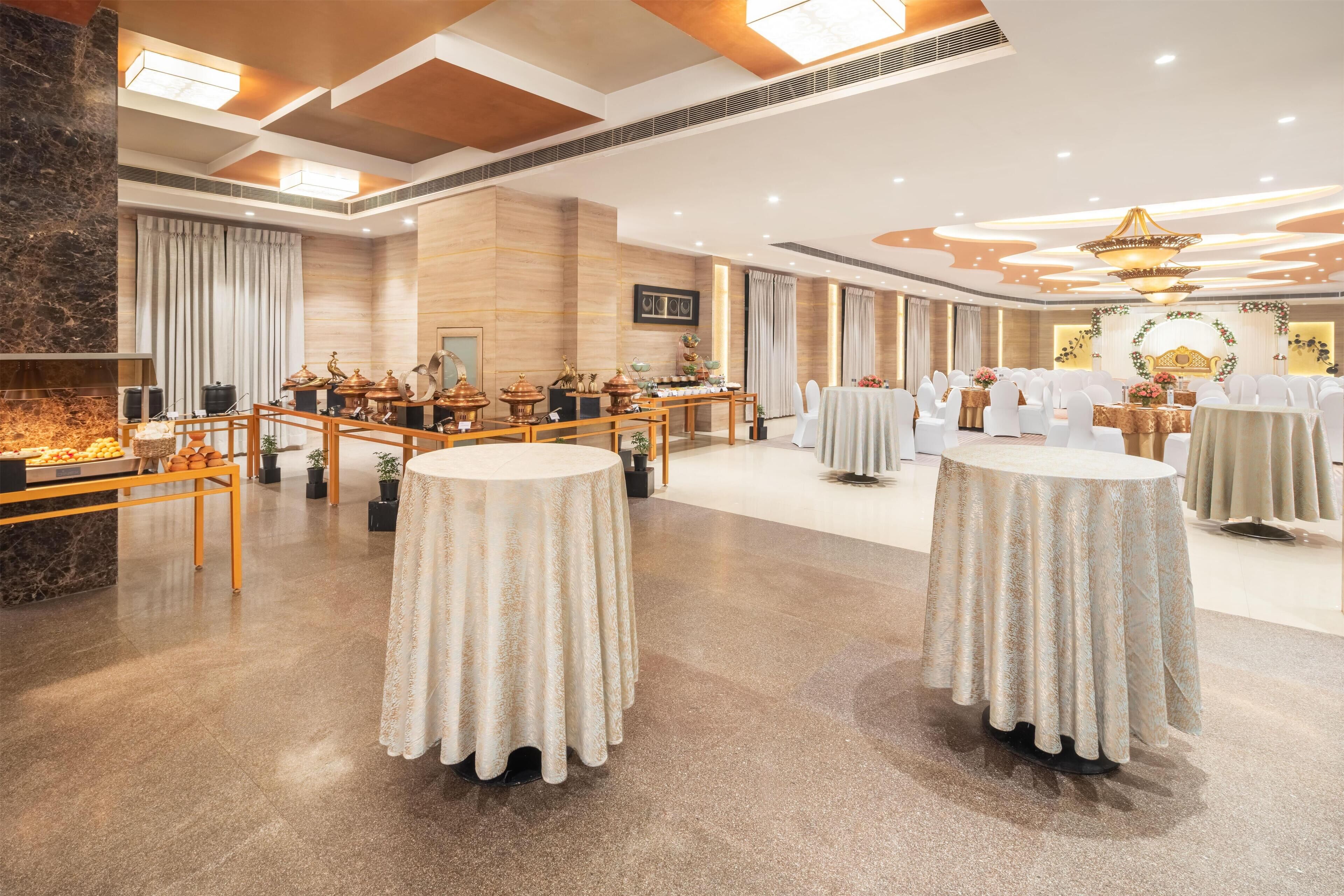 A spacious banquet hall with round tables, a stage, and a decorative arch.