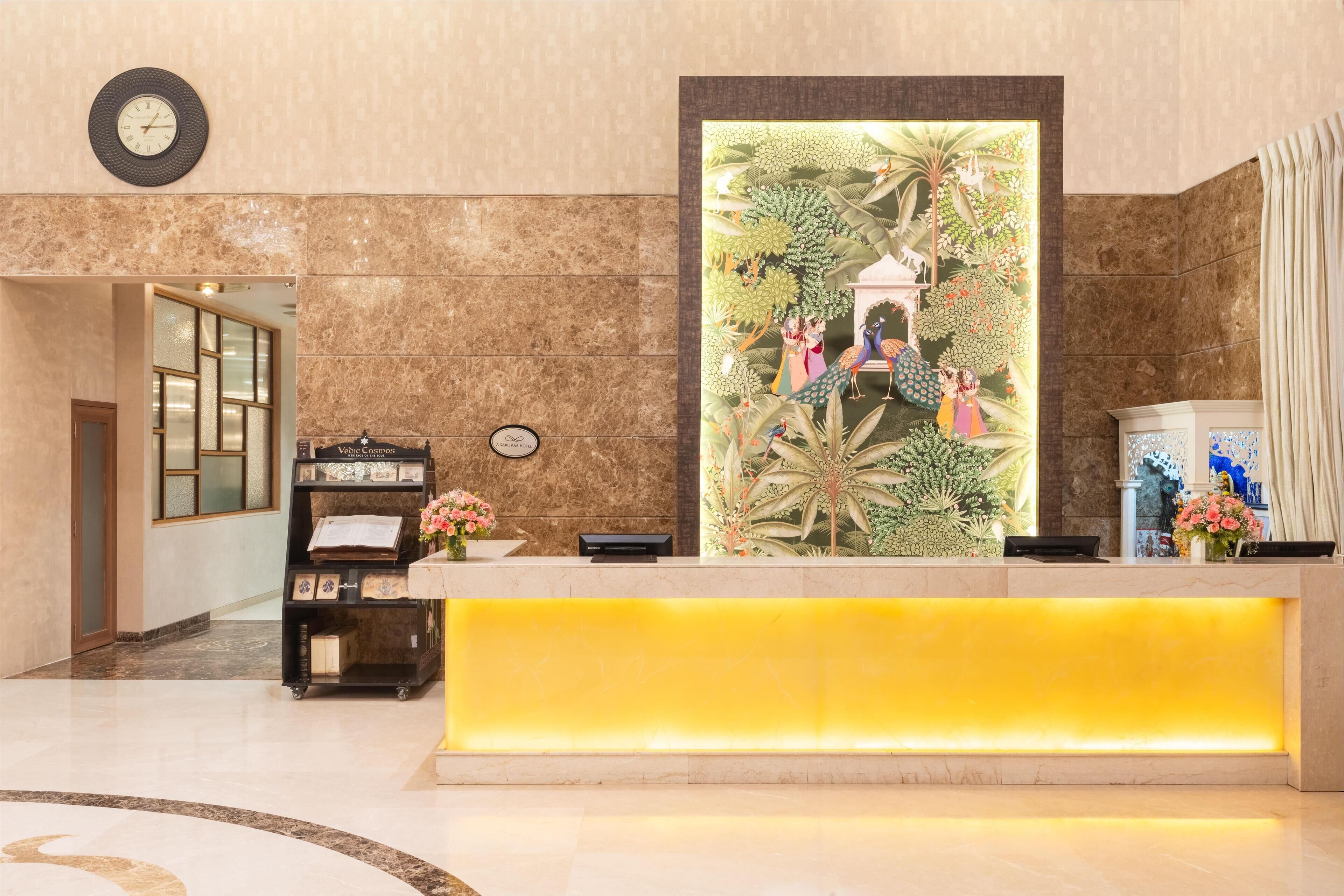 A reception area with a marble wall, a clock, a reception desk with a yellow accent, and a large decorative mural.